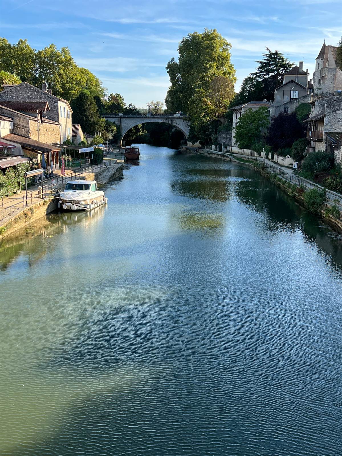 La Baïse à Nérac, bordée d’arbres, avec le pont de pierre en arrière-plan.