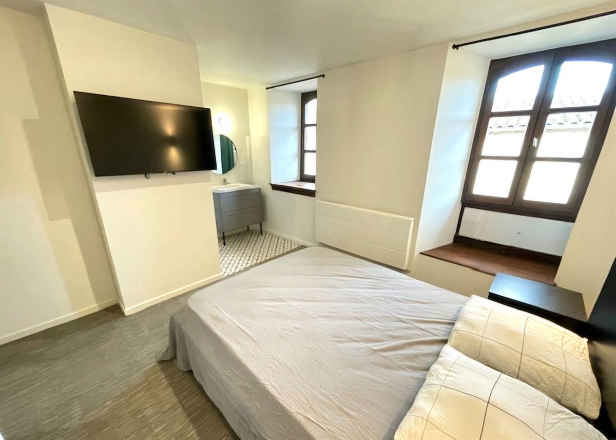 Chambre avec télévision murale, fenêtre à petits carreaux et lit double.