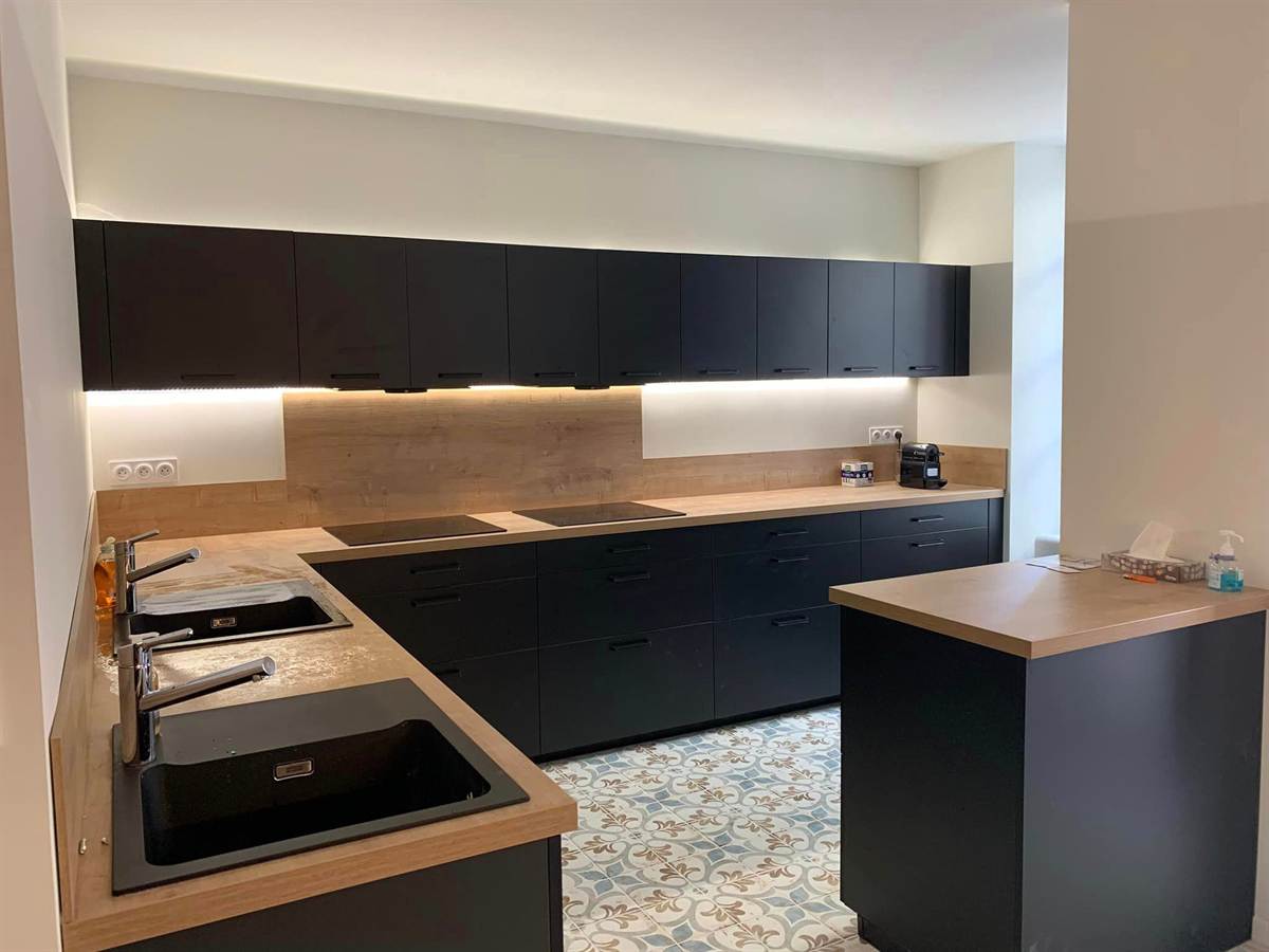 Cuisine noire à plans de travail bois, avec deux éviers et deux zones de cuisson.