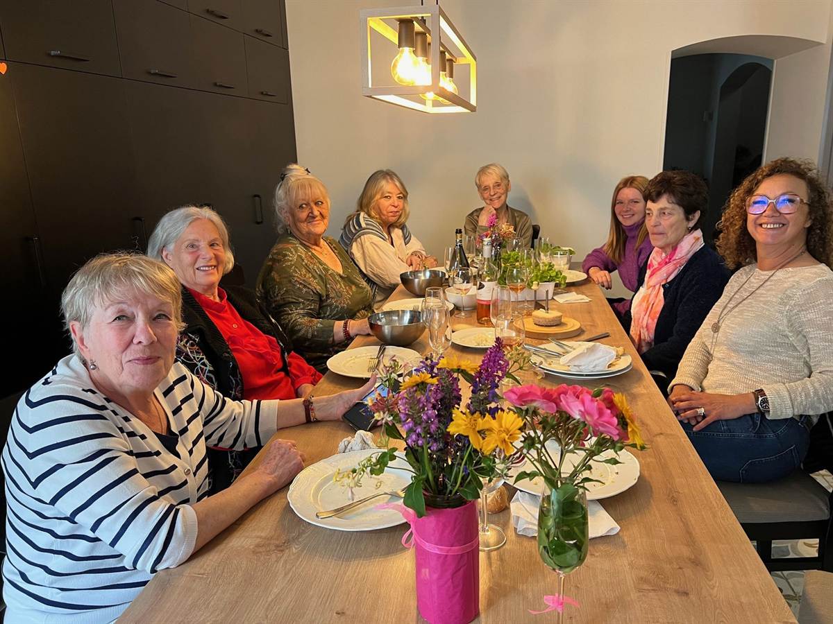 Huit habitantes et amies attablées autour d’un repas, avec des fleurs sur la grande table.