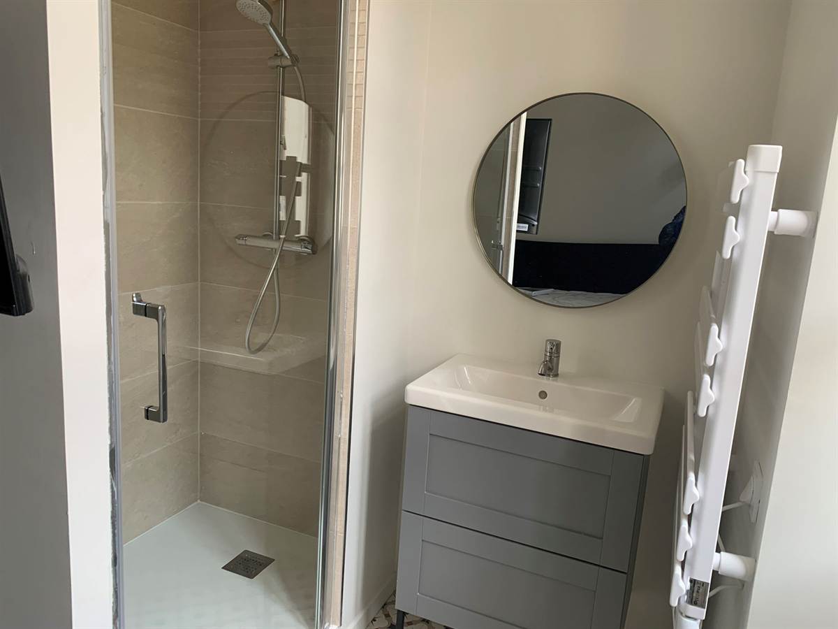 Salle d’eau privative avec douche à l’italienne, meuble vasque et miroir rond.